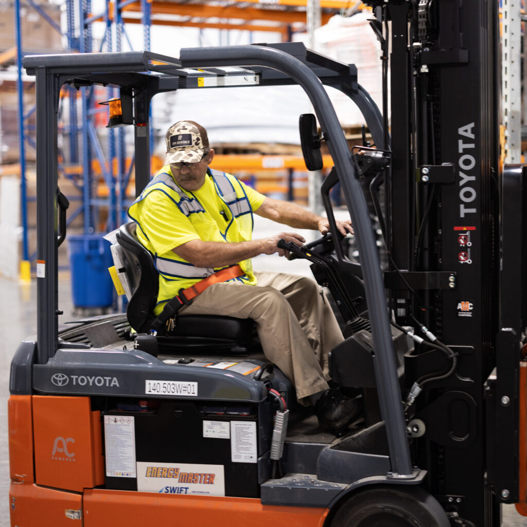 Warehouse worker in a high vis vest and safety glasses driving a forklift